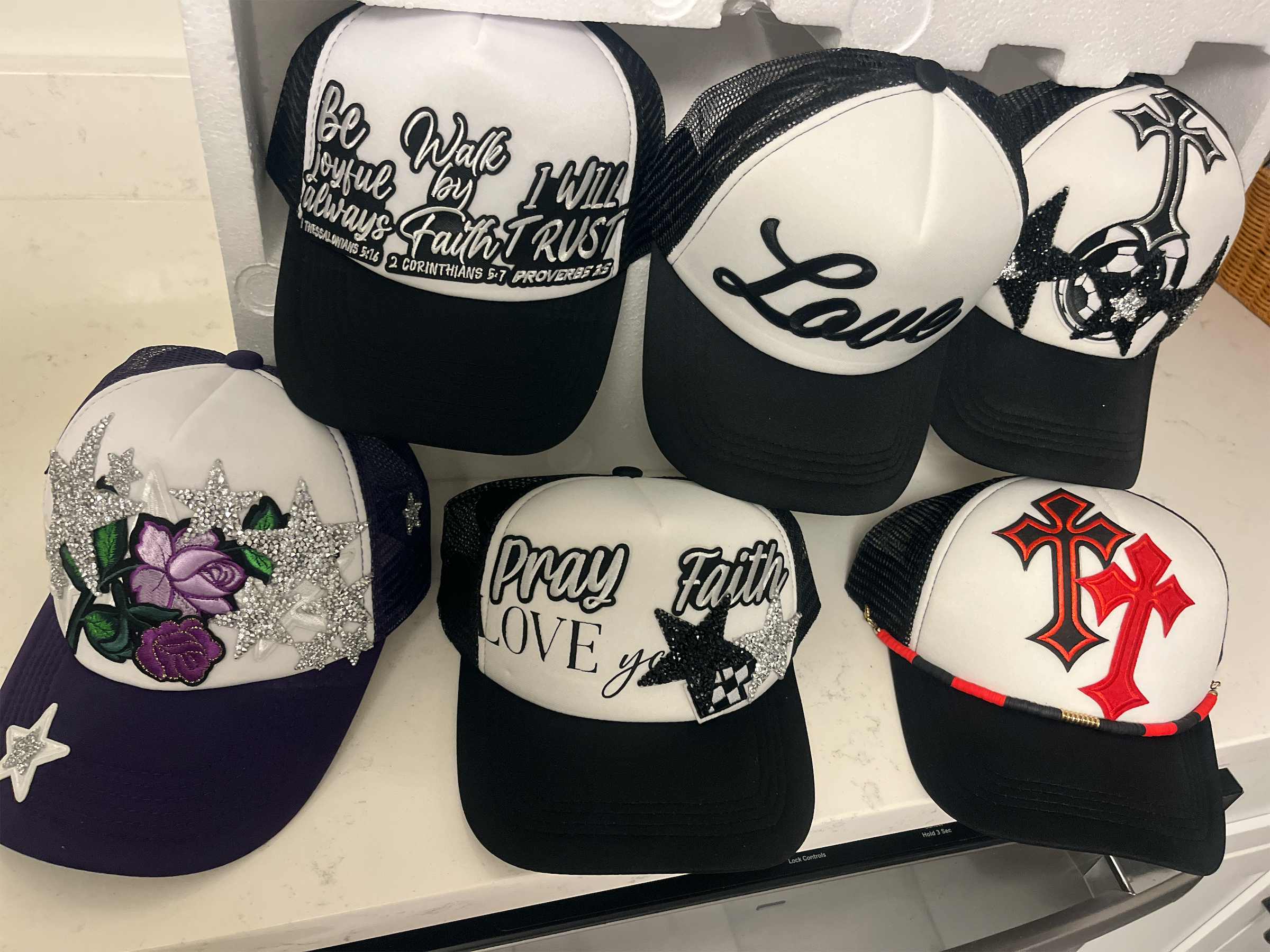 Peacefulcornerapparel collection of black and white trucker hats with faith-inspired embroidery and rhinestone motifs.